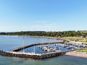 A marina with boats docked, surrounded by a rocky breakwater and a forested landscape in the background. - "Gertina" - 100m from the sea by Interhome (Knebel)