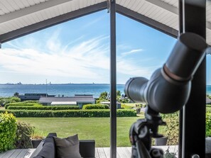 Ett takförsett utomhusområde med utsikt över havet, ett teleskop och välklippta häckar.