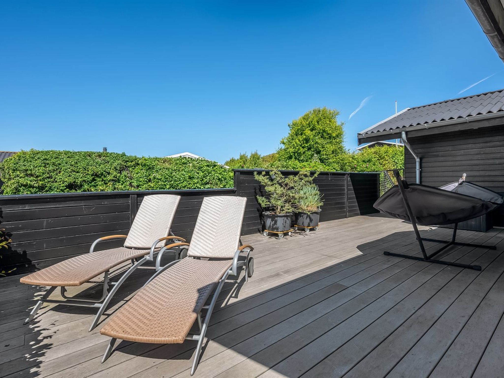 A deck with lounge chairs, a grill, and potted plants.