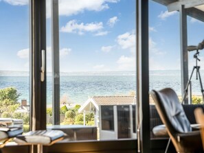 A room with large windows overlooking a body of water, a chair, and a tripod. - "Gertina" - 100m from the sea by Interhome (Knebel)
