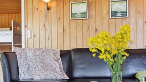 Un sofá de cuero negro con un cojín floral, un florero con flores amarillas y dos cuadros en una pared de madera.