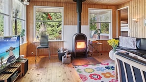 Un acogedor interior de cabaña con estufa de leña, televisor y una zona de estar confortable.