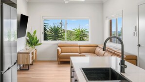 Una cocina moderna con estufa integrada, un amplio ventanal con vistas a zonas verdes, y un sofá de cuero en la sala de estar.