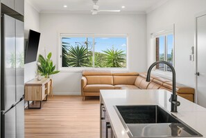 Una cocina moderna con estufa integrada, un amplio ventanal con vistas a zonas verdes, y un sofá de cuero en la sala de estar.