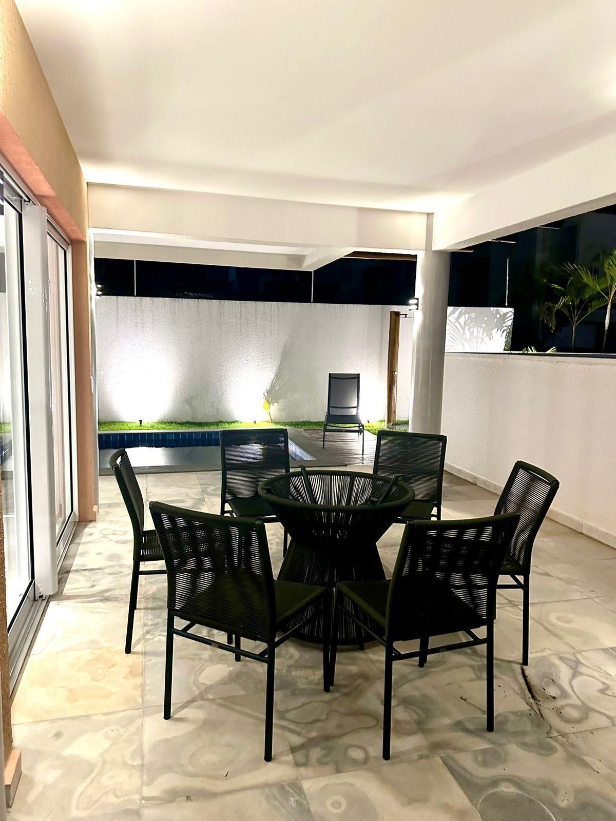 Un'area pranzo esterna moderna con un tavolo rotondo e sedie, un ingresso con porta in vetro e vista su un giardino curato.
