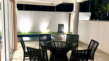 Un'area pranzo esterna moderna con un tavolo rotondo e sedie, un ingresso con porta in vetro e vista su un giardino curato.