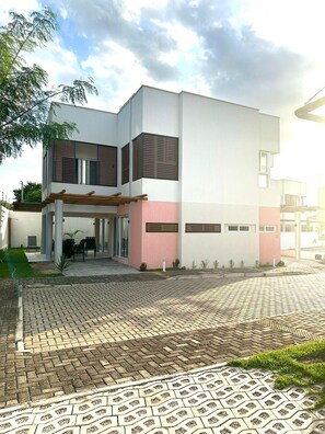 A modern two-story building with a flat roof, large windows, and a paved driveway.