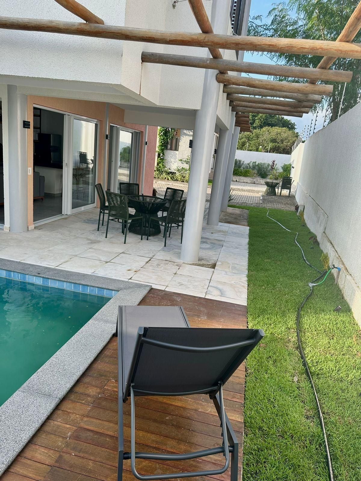 Uma área externa coberta com piscina, móveis de jardim e gramado.