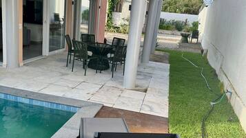Uma área externa coberta com piscina, móveis de jardim e gramado.
