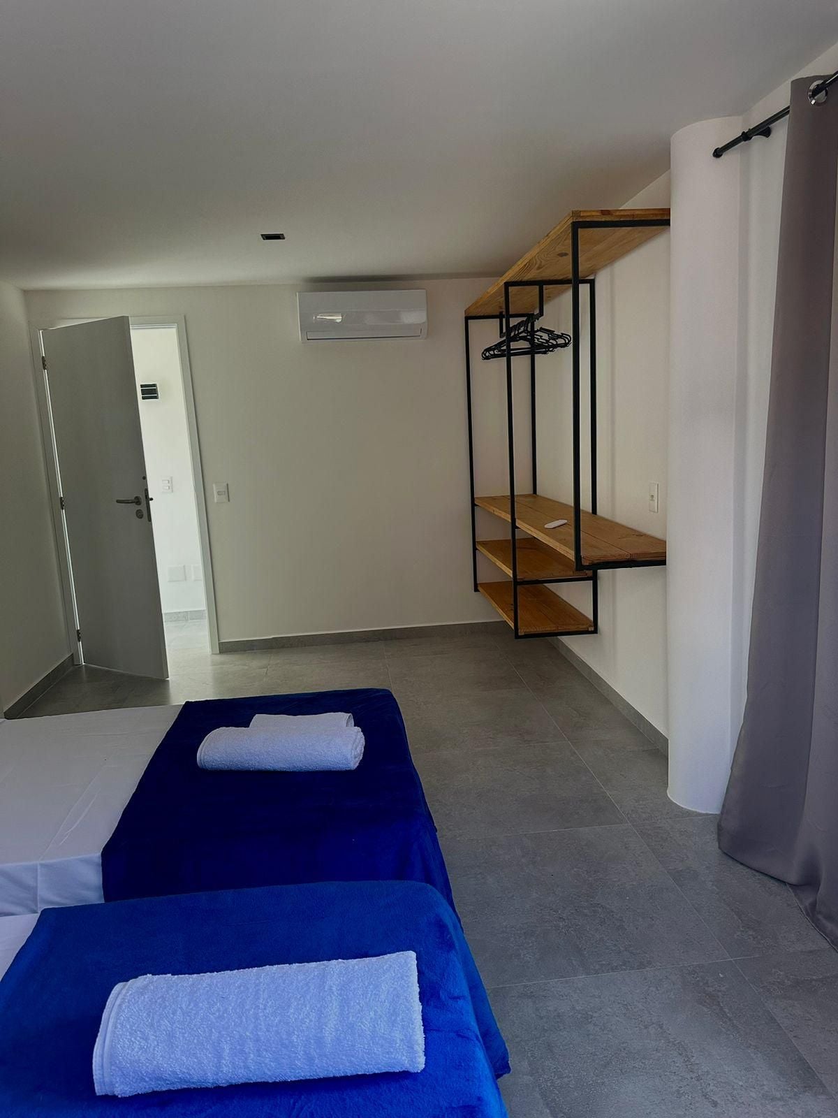 A hotel room with a bed, a wardrobe, a hanging rack, and a door leading to another room.