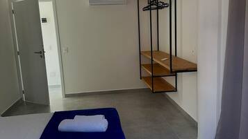 A hotel room with a bed, a wardrobe, a hanging rack, and a door leading to another room.