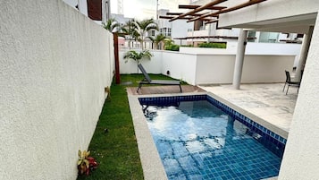 Un espacio al aire libre residencial con piscina, césped y un muro blanco.