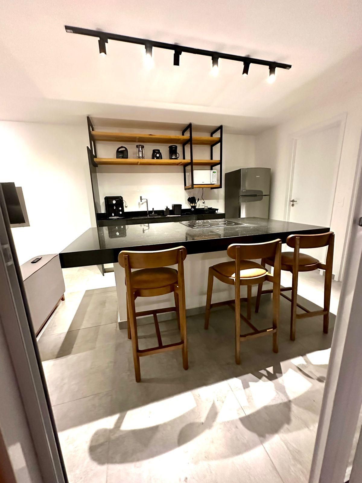 A modern kitchen with a black countertop, wooden chairs, and a built-in oven.