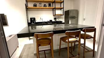 A modern kitchen with a black countertop, wooden chairs, and a built-in oven.