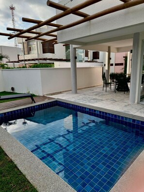 A swimming pool with a tiled edge, surrounded by a patio area with chairs and a table. - Praia da Pipa - Mar e Descanso (Tibau do Sul)
