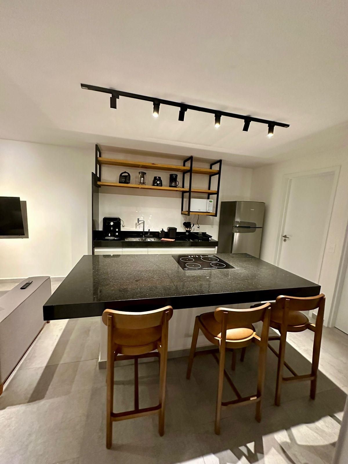 A modern kitchen with a central island, wooden chairs, a built-in oven, and a coffee machine.