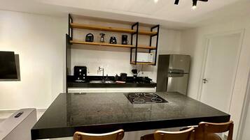 A modern kitchen with a central island, wooden chairs, a built-in oven, and a coffee machine.
