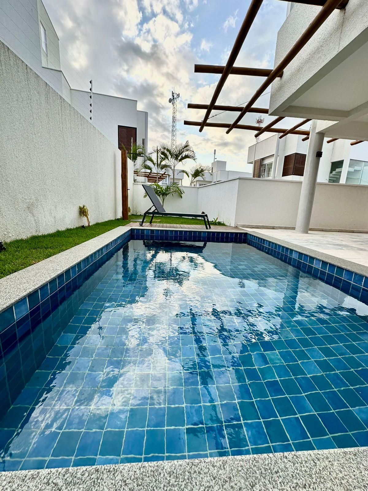 Une piscine dont le bord est revêtu de carrelage, entourée d’un mur blanc et agrémentée d’une pergola en bois.