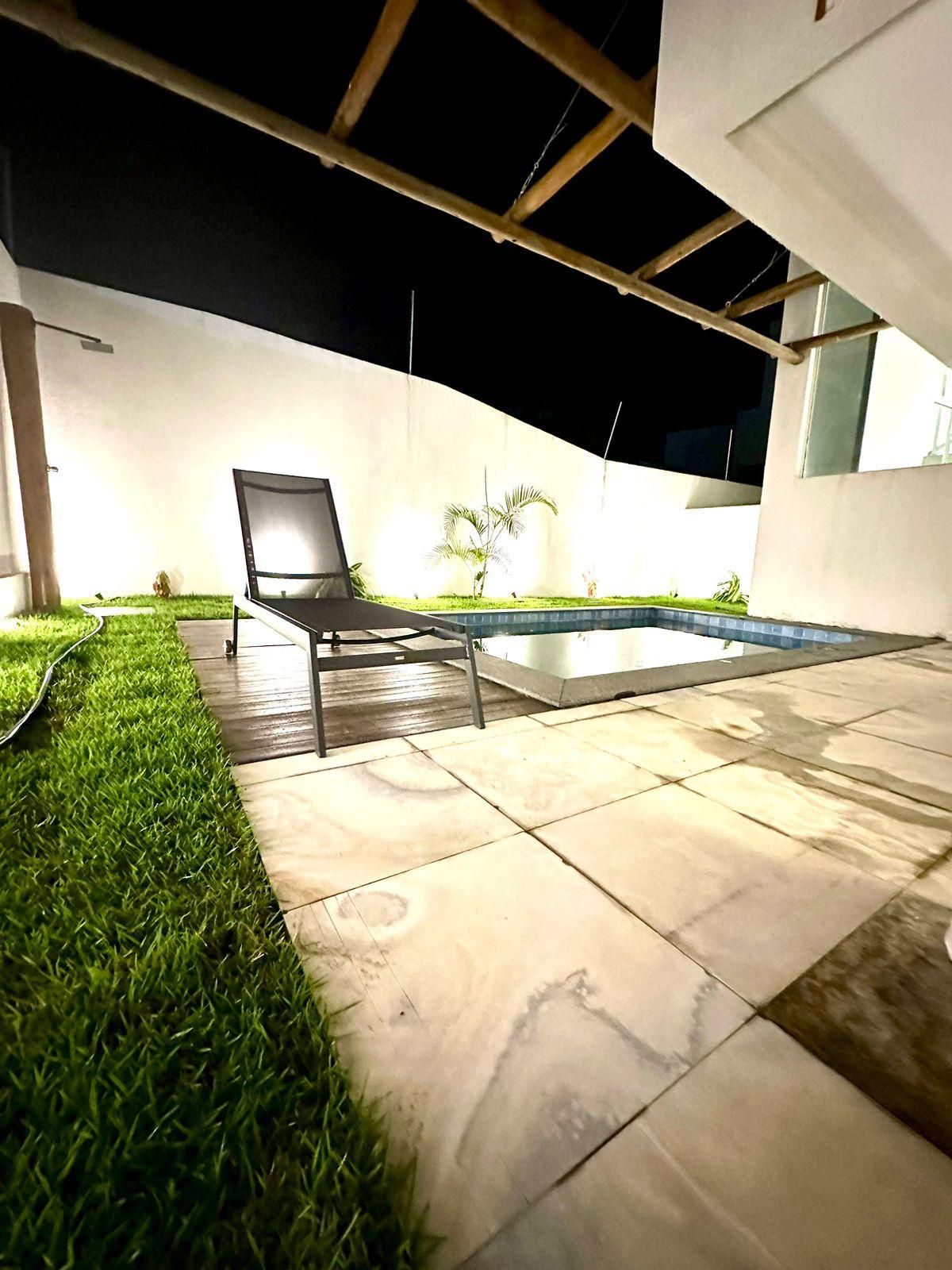Uma área externa moderna com piscina, espreguiçadeira e gramado bem cuidado.