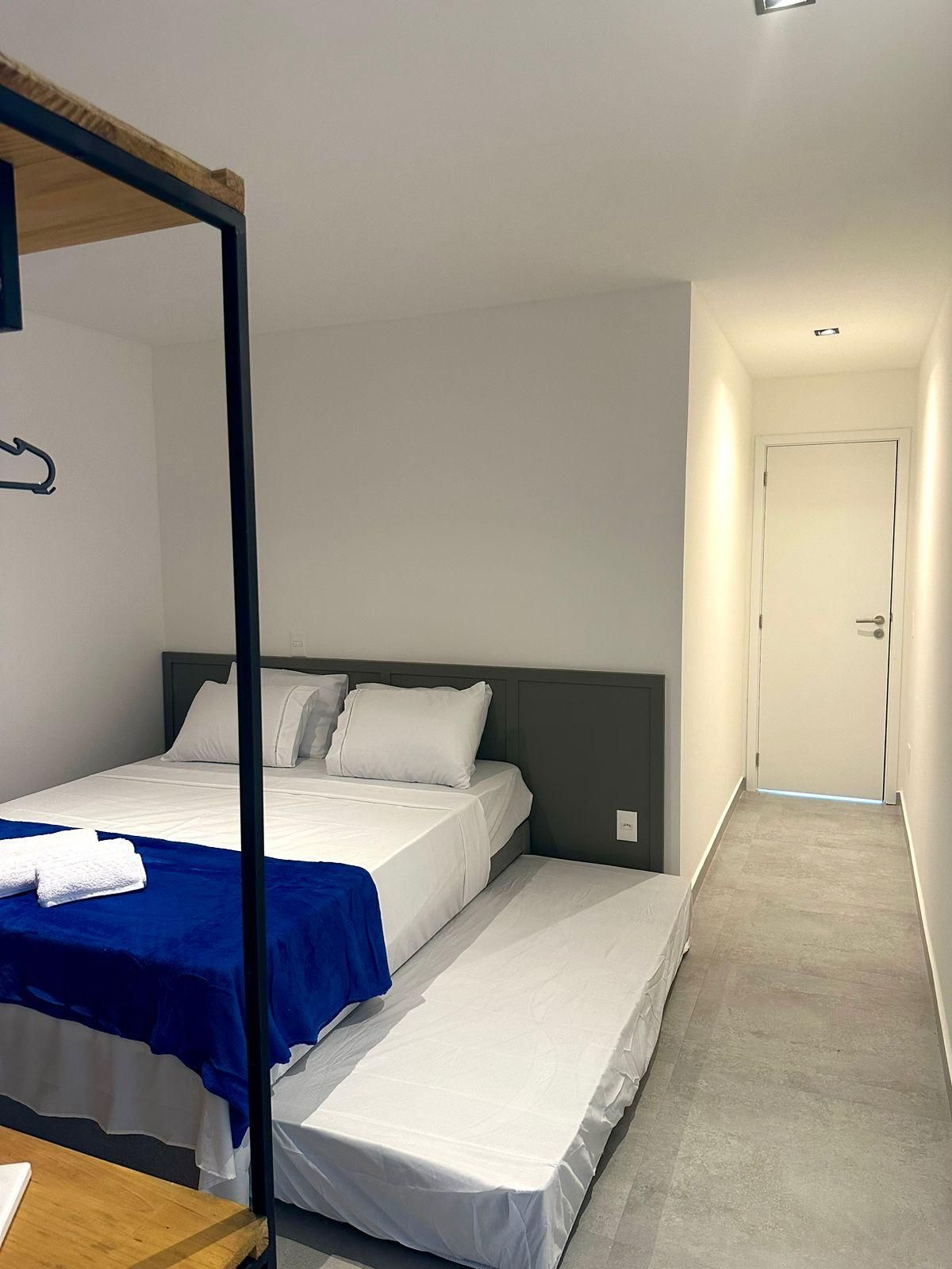 Une chambre d’hôtel avec un lit, une table en bois, un porte-manteau mural et une porte donnant sur une autre pièce.