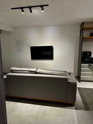 A modern living room with a sofa, a flat-screen TV mounted on the wall, and a coffee machine on a counter. - Praia da Pipa - Mar e Descanso (Tibau do Sul)