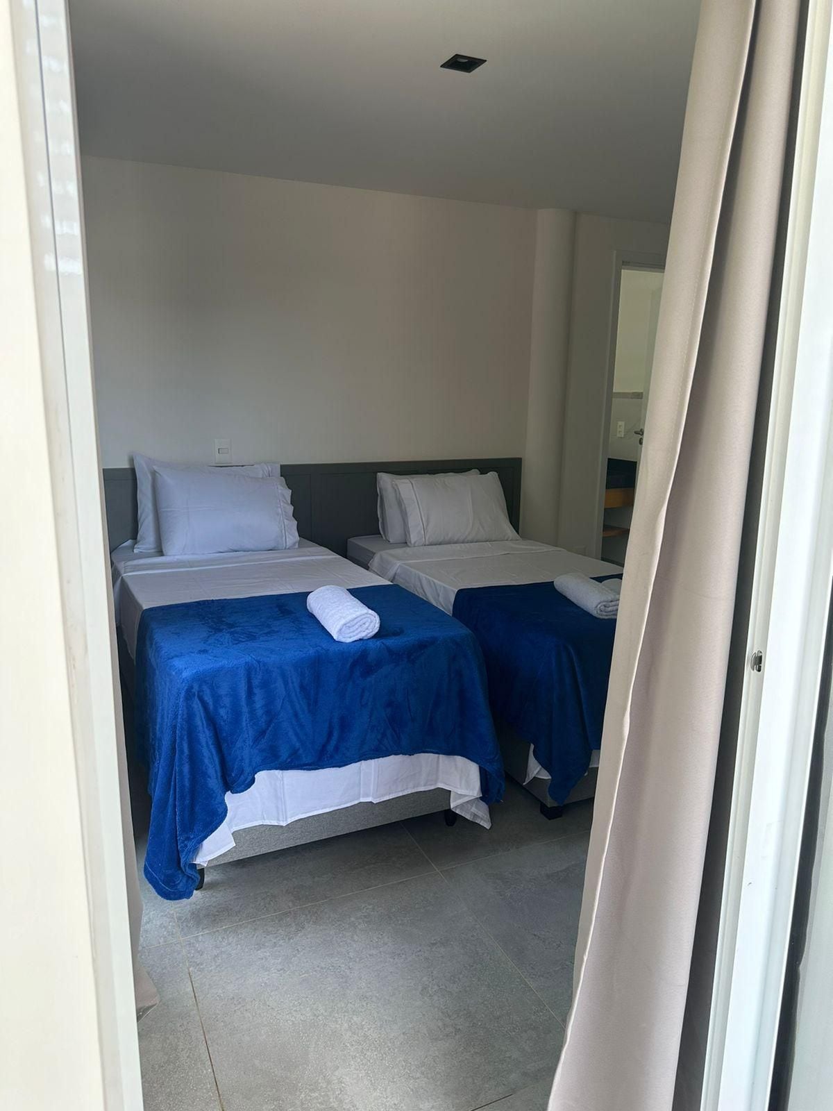 A hotel room with two beds, each with a white pillow and a blue bedspread.