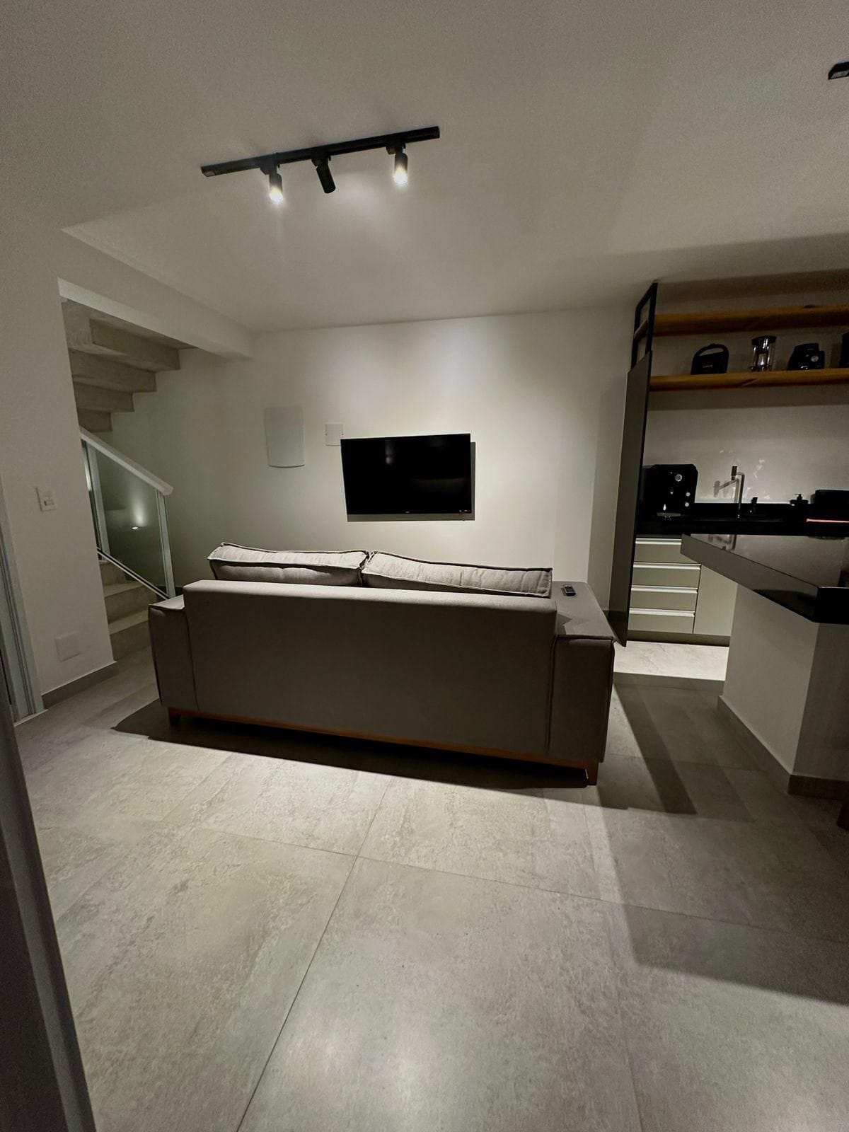 A modern living room with a sofa, a flat-screen TV mounted on the wall, and a staircase leading to another level.