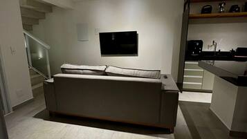 A modern living room with a sofa, a flat-screen TV mounted on the wall, and a staircase leading to another level.