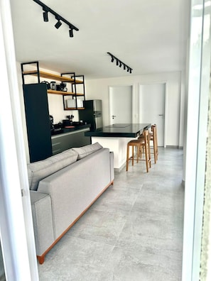 A modern kitchen with a central island, a dining area with wooden chairs, and a grey sofa.