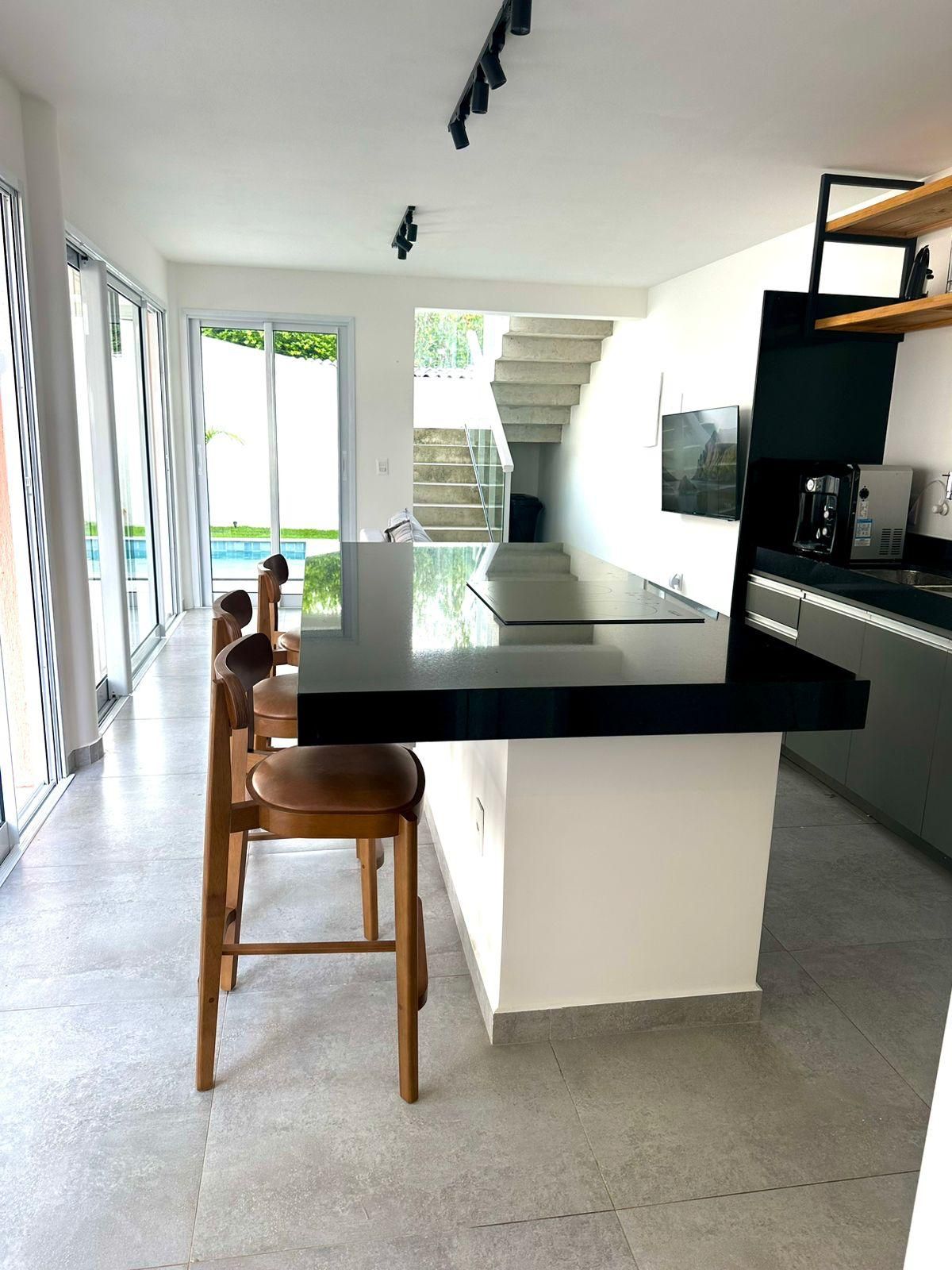 A modern kitchen with a large island, bar stools, a coffee machine, and a view of a staircase leading to a balcony.