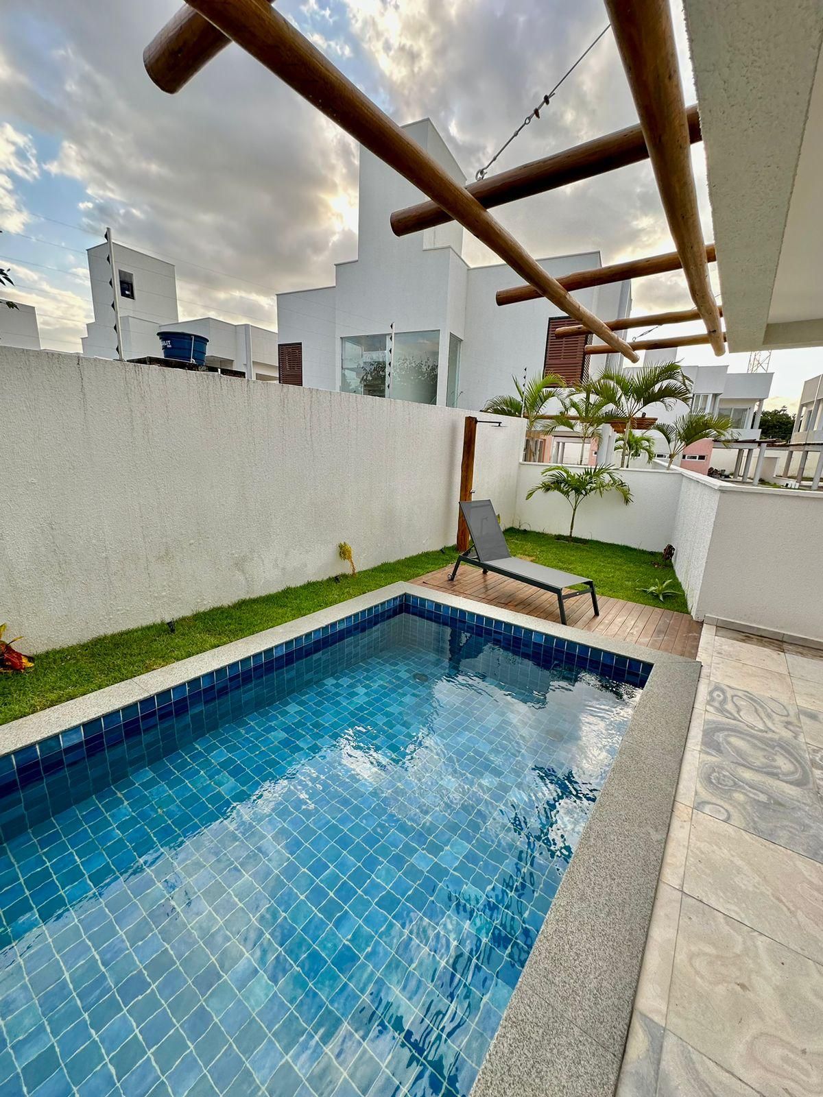 Piscina com borda azulejada, cercada por um muro branco e gramado.