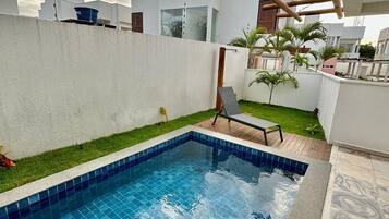 Piscina com borda azulejada, cercada por um muro branco e gramado.