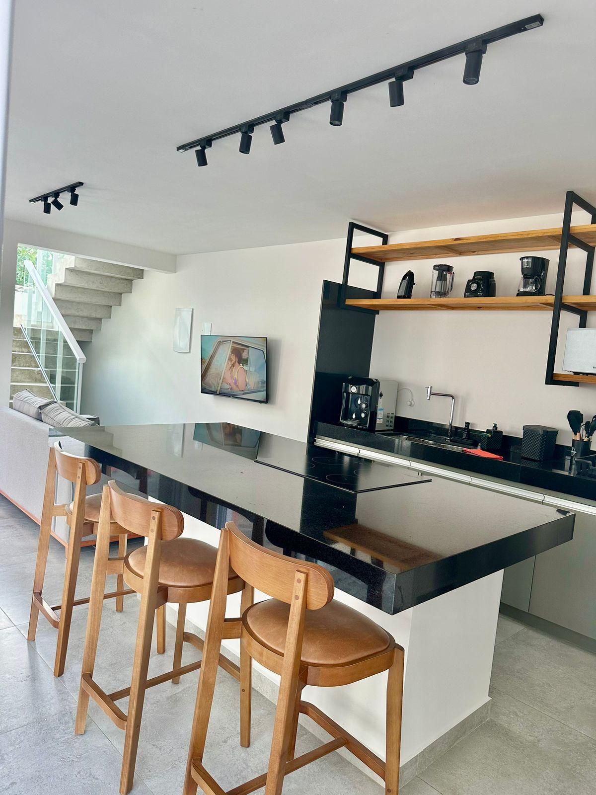 Uma cozinha moderna com uma ilha central, banquetas de bar, cafeteira e televisão.