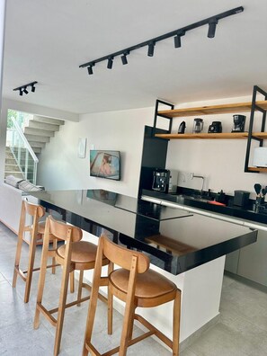 A modern kitchen with a central island, bar stools, a coffee machine, and a television.