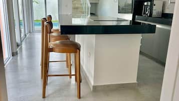 A modern kitchen with a central island, bar stools, and a staircase leading to an outdoor area.