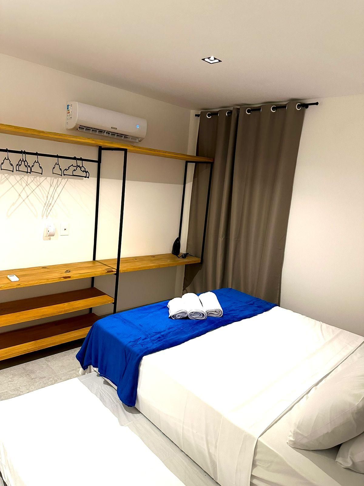 Un dormitorio con literas, una colcha azul, ropa de cama blanca, un estante de madera y un aire acondicionado de pared.