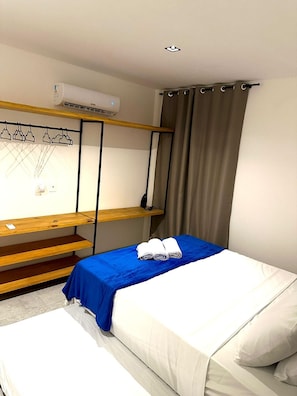 A bedroom with a bunk bed, a blue bedspread, white bedding, a wooden shelf, and a wall-mounted air conditioner. - Praia da Pipa - Mar e Descanso (Tibau do Sul)
