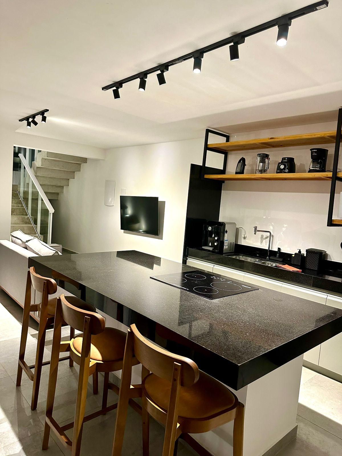 Cozinha moderna com ilha central, banquetas, forno embutido e máquina de café.