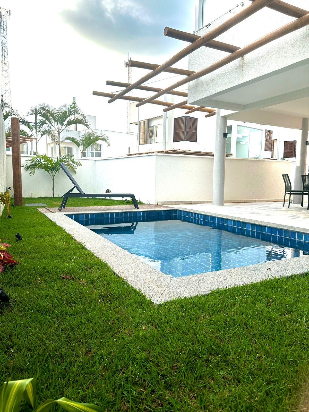 A swimming pool with a tiled edge, surrounded by grass, and a pergola structure overhead.