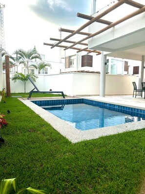 A swimming pool with a tiled edge, surrounded by grass, and a pergola structure overhead. - Praia da Pipa - Mar e Descanso (Tibau do Sul)