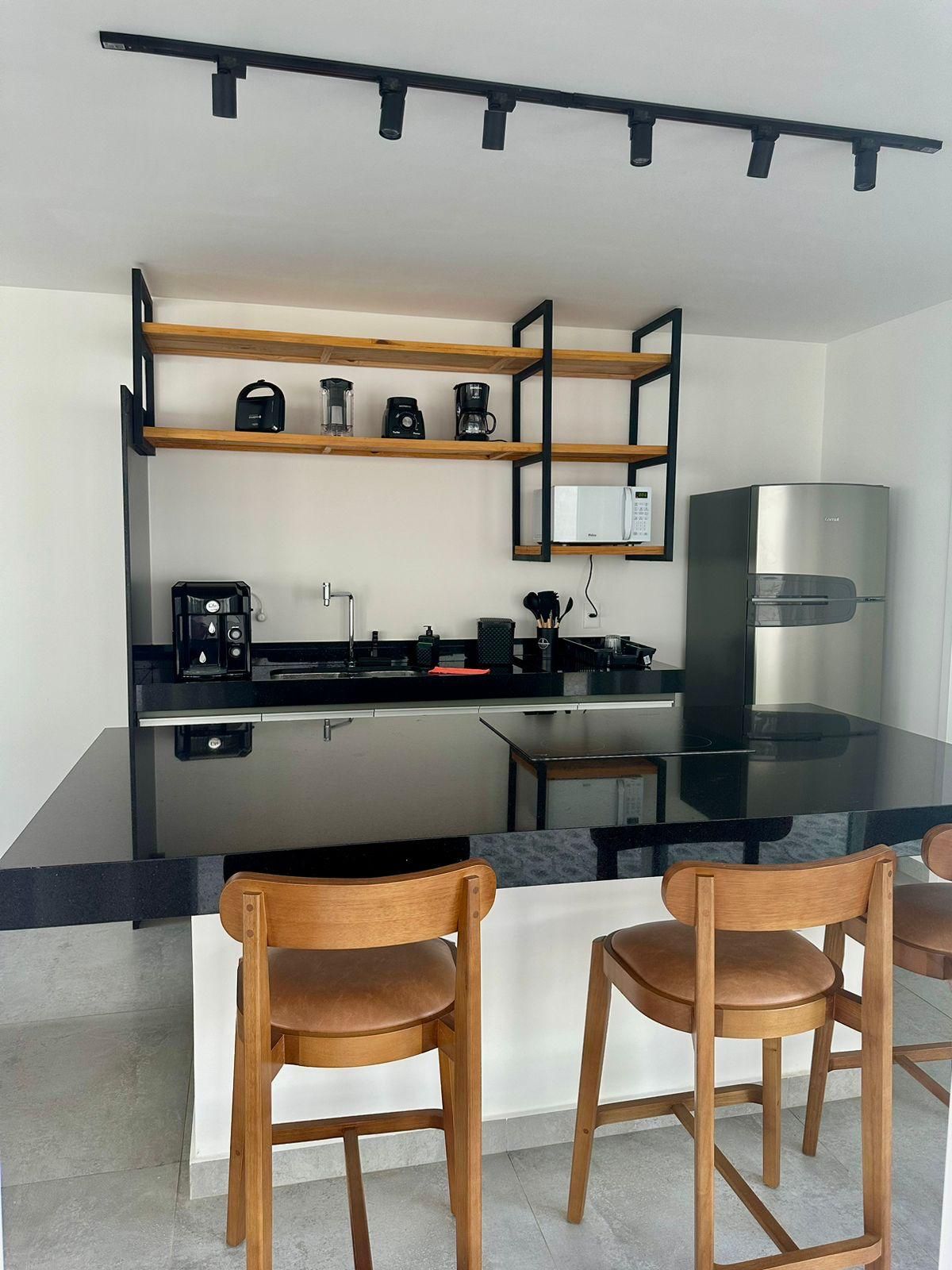Cozinha moderna com ilha central, cadeiras de madeira e micro-ondas embutido.