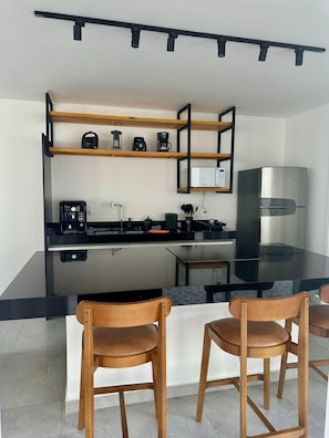 A modern kitchen with a central island, wooden chairs, and a built-in microwave. - Praia da Pipa - Mar e Descanso (Tibau do Sul)