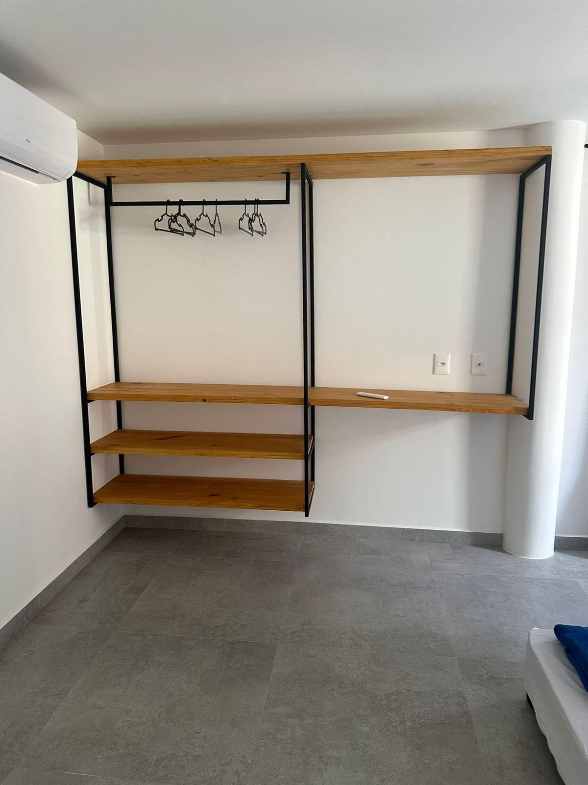 Quarto com estante embutida, com três prateleiras de madeira e um cabideiro.