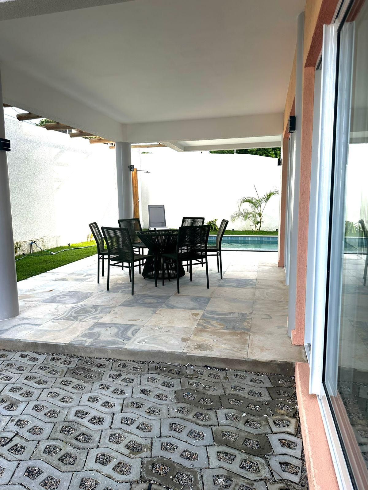 Área de varanda coberta com mesa e cadeiras, piso em azulejo e vista para uma piscina.