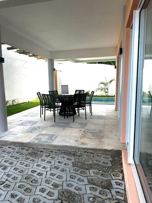 A covered patio area with a table and chairs, a tiled floor, and a view of a swimming pool.