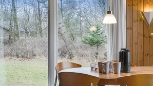 Ein Essbereich mit Tisch, Stühlen und Blick auf ein bewaldetes Gebiet durch große Fenster.