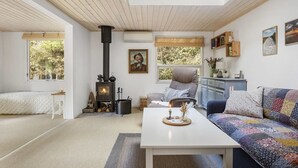 A cozy living room with a wooden ceiling, a fireplace, a sofa, a table, and a window with a view of trees. - "Ansfried" - 900m from the sea by Interhome (Sæby)