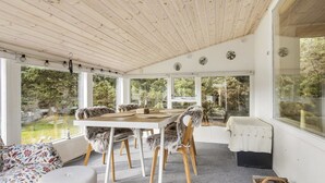A room with a wooden ceiling, a dining table with chairs, a sofa, and a window with a view of greenery. - "Ansfried" - 900m from the sea by Interhome (Sæby)