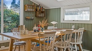 A dining area with a wooden table, chairs, a vase with dried plants, and a window with a view of greenery. - "Bedrija" -  from the sea by Interhome (Hals)