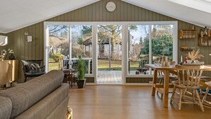 A spacious living area with a high ceiling, a large sliding glass door leading to a backyard, a wooden dining table with chairs, and a cozy sofa. - "Bedrija" -  from the sea by Interhome (Hals)
